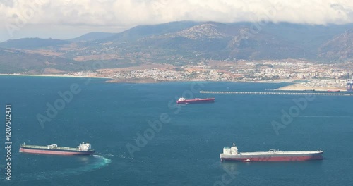 View from Gibraltar, British Overseas Territory and city on the Iberian Peninsula. Three large tankers at sea near a coastal city and mountains.
