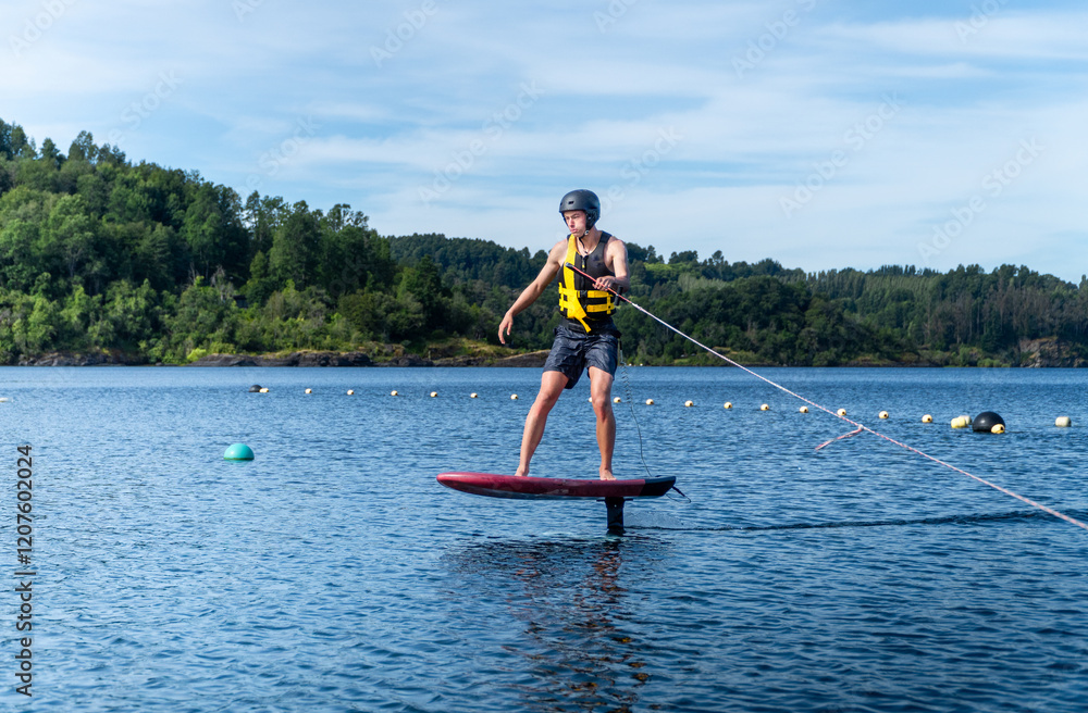 A young surfer riding a foil board, skillfully gliding over the water while being towed by a boat on a serene lake.