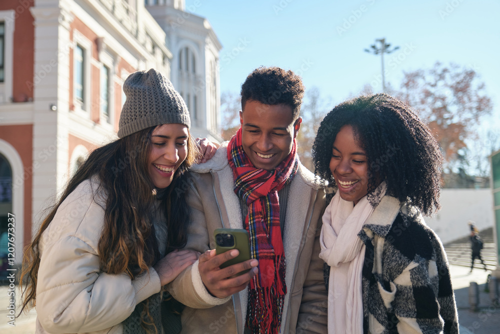 Three joyful young students are using mobile phone and enjoying sunny winter day in Madrid, Spain