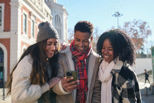 Obraz na płótnie Three joyful young students are using mobile phone and enjoying sunny winter day in Madrid, Spain w salonie