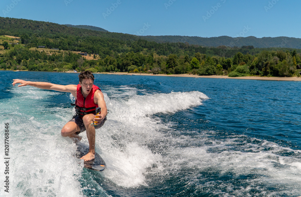 A cheerful young wake surfer in swimwear and a life vest filming himself with an action camera while gliding over the water, enjoying the thrill of the sport. A cheerful young wake surfer in swimwear and a life vest filming himself with an action camera while gliding over the water, enjoying the thrill of the sport.