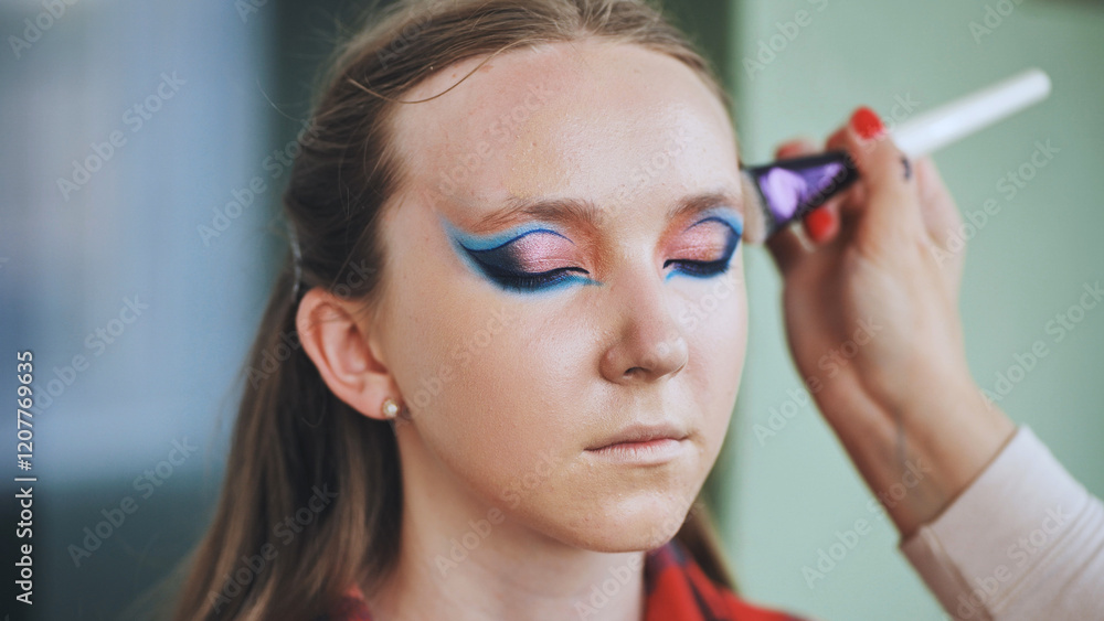 Professional makeup artist applying fantasy makeup on a young model's face using a brush, creating a colorful and artistic look Professional makeup artist applying fantasy makeup on a young model's face using a brush, creating a colorful and artistic look