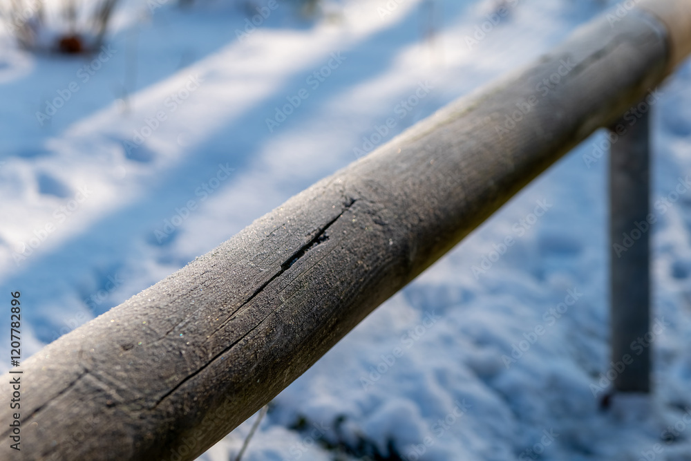 Fototapeta premium Frost-covered wooden railing in a tranquil winter landscape under soft sunlight