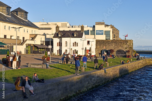 Young people sitting on the banks at the mouth of the Corrib River, downtown Galway, Connemara, County Galway, Connacht, Republic of Ireland photo