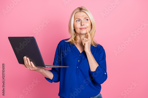 Photo portrait of pretty senior female hold netbook look skeptical empty space wear trendy blue outfit isolated on pink color background photo