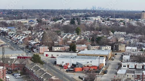 Aerial approaching shot of cars on main street with industrial factory. Townhouses in american city during sunny winter day. Tilt up wide shot. Skyline of Philadelphia in distance. photo