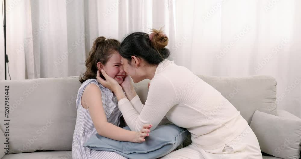 Asian mother and daughter smiling warmly while touching foreheads on sofa. Scene conveys deep love, trust, and bonding, highlighting familial affection in a cozy and intimate home setting. Asian mother and daughter smiling warmly while touching foreheads on sofa. Scene conveys deep love, trust, and bonding, highlighting familial affection in a cozy and intimate home setting.