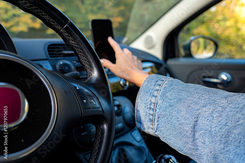 Inside the car, from her point of view, the woman touches the phone on the support, making sure the map shows the correct route photo