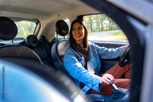 A young woman, smiling, holds the gear shift with one hand while driving photo