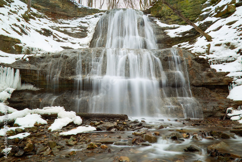 A long exposure blurred motion gorgeous cascading waterfall in the late winter, early spring, with melting snow and ice.