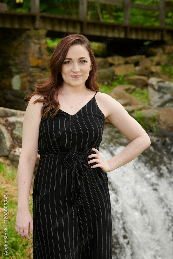 Stunning young woman in black jumper or romper poses for portrait near cascade in park Stunning young woman in black jumper or romper poses for portrait near cascade in park