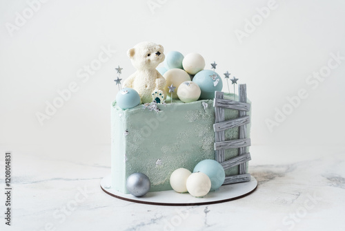 Trendy half of cake with blue chocolate coating decorated with teddy bear on top. Birthday cake for a little baby with chocolate turquoise and silver spheres on white background. 6 month celebration. photo