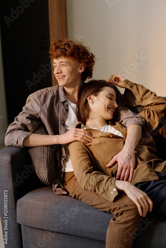 Vertical shot of comfortable couch with young adult coupe resting and chatting while room illumed with warm golden sunrays photo