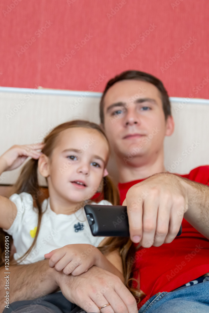 Cheerful small girl daughter and her handsome young dad spending time together watching TV at home. Cheerful small girl daughter and her handsome young dad spending time together watching TV at home.