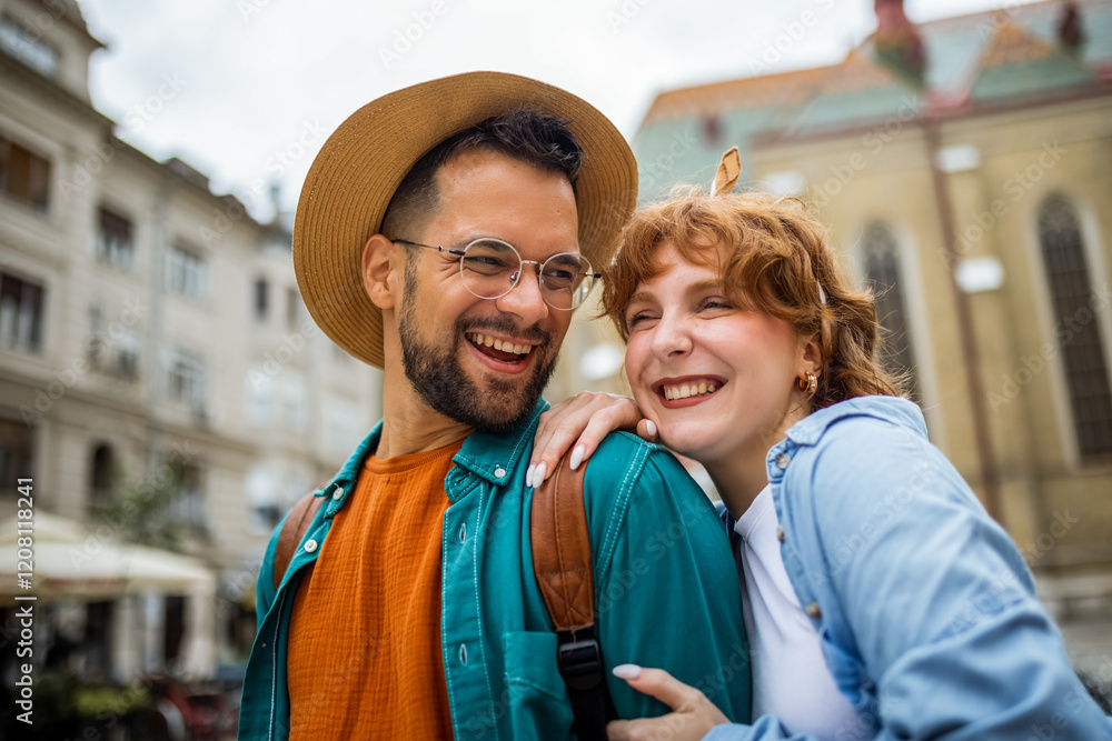 Naklejka premium Young couple exploring the new city. Hugging and walking through the center. Wearing hats and backpacks.