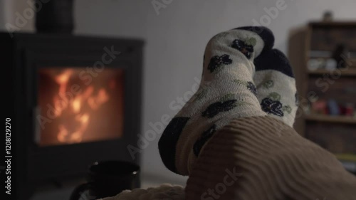 horizontal video of bare feet of a woman with patterned sock resting on a pouf in front of a wood fireplace