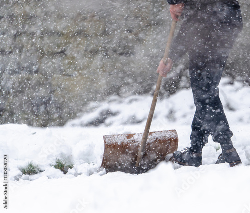 A man is shoveling snow with a wooden handle