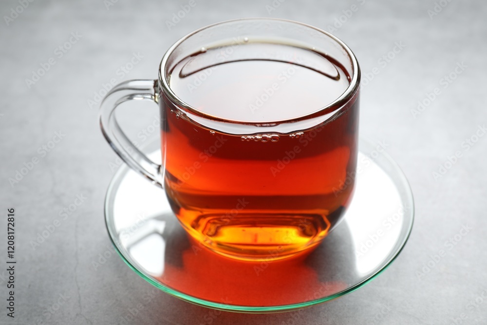 Refreshing black tea in cup on grey textured table, closeup Refreshing black tea in cup on grey textured table, closeup