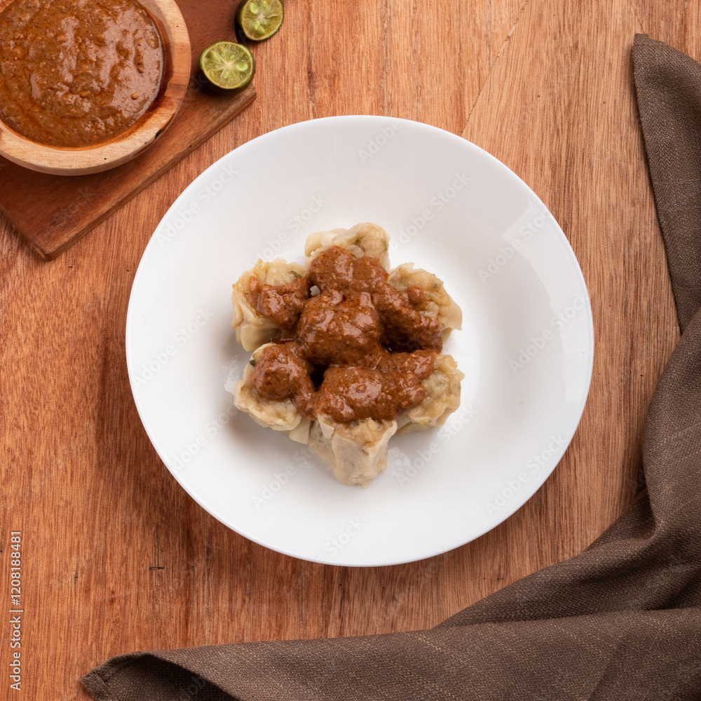 Delicious dumplings topped with a rich sauce sit on a white plate with lime halves nearby on a rustic wooden table Delicious dumplings topped with a rich sauce sit on a white plate with lime halves nearby on a rustic wooden table