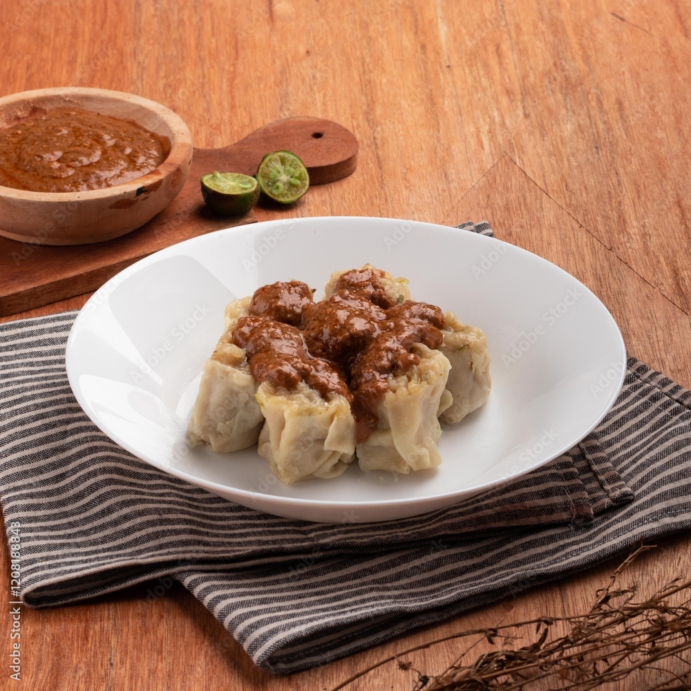 Steamed dumplings topped with rich sauce and served with lime halves on a textured wooden surface, perfect for a flavorful meal