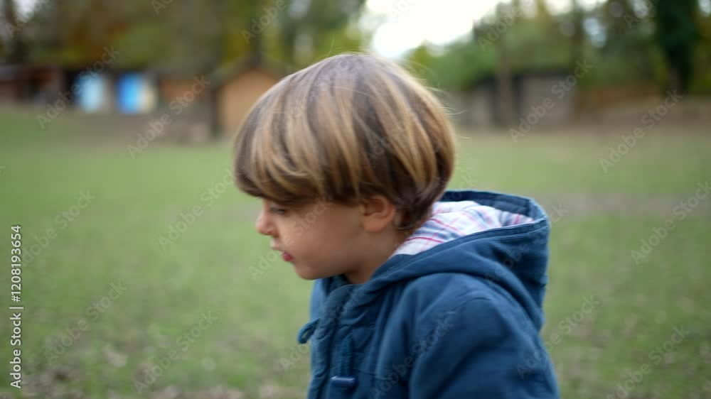 Profile of small 4 year old boy walking outside at outdoor park wearing jacket during autumn fall season, active pensive kid enjoys nature, walks forward Profile of small 4 year old boy walking outside at outdoor park wearing jacket during autumn fall season, active pensive kid enjoys nature, walks forward