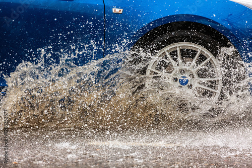 Принти на полотні Blue car driving through a puddle on a flooded road with water and splashes caused by heavy rain