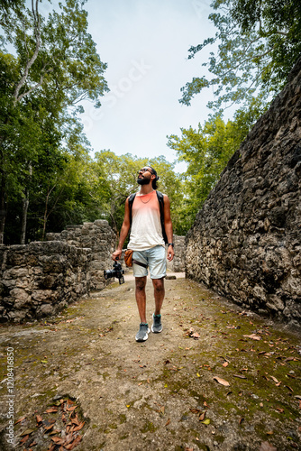 Hombre joven viajero visitando el sitio arqueológico de Cobá en México, rodeado de selva y ruinas, turista disfrutando de la vista de las pirámides photo