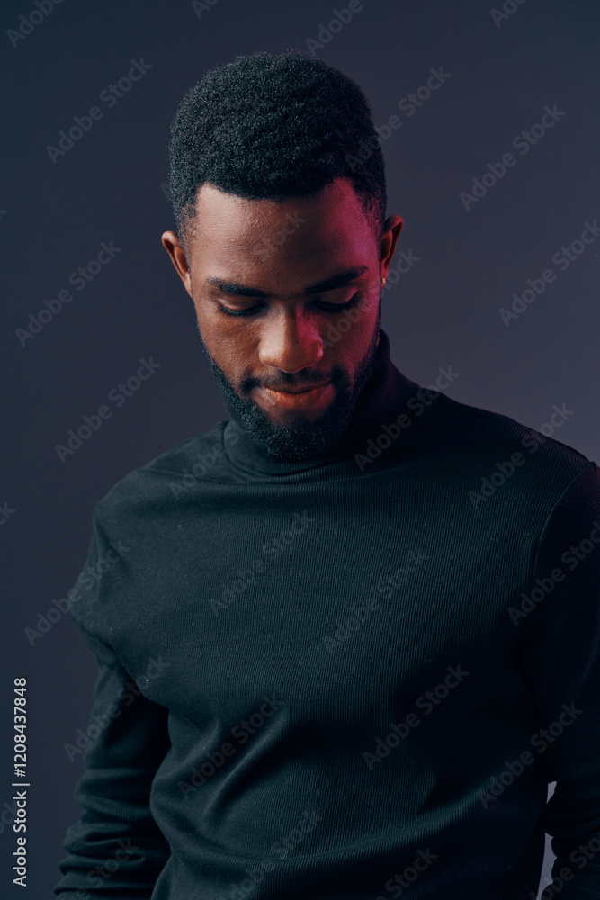 Fototapeta premium A thoughtful young African man in a black turtleneck sweater looking down against a dark gradient background, conveying introspection and calm emotions