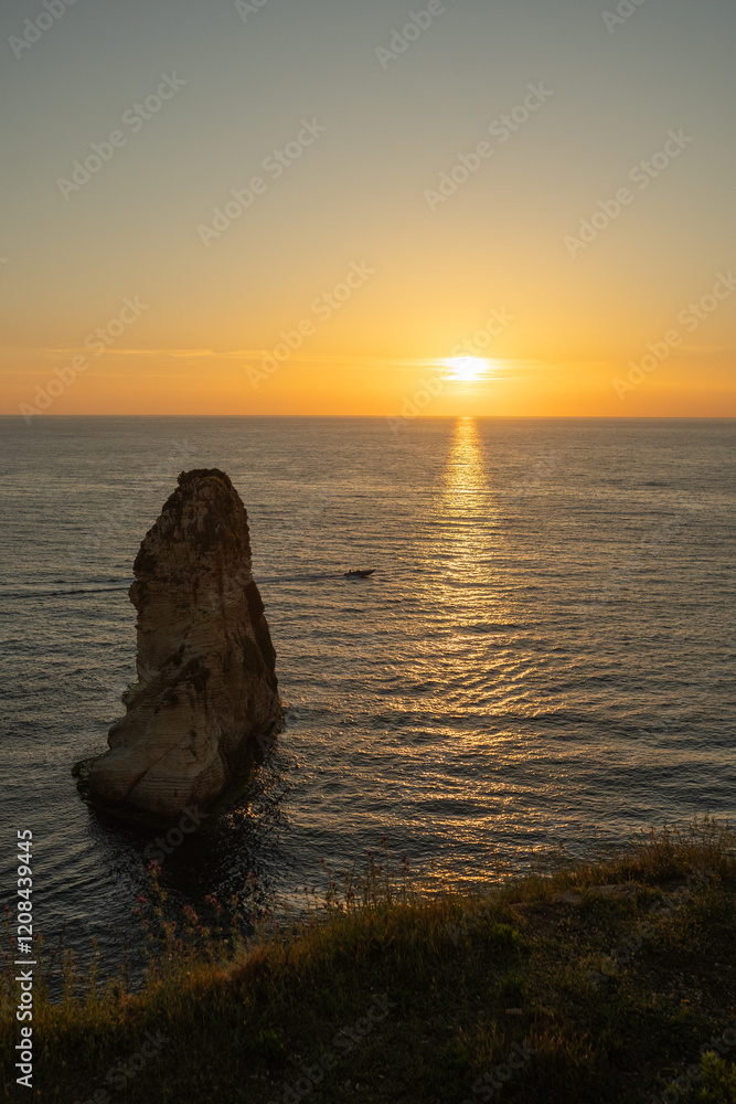 Fototapeta premium The sunset behind Raouche Rock in Lebanon, casting a stunning glow over the Mediterranean waters. Travel blogs, postcards, and tourism advertisements, social media content.