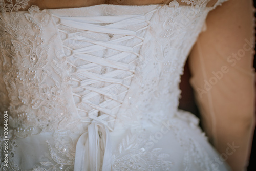 A close-up of the back of a lace wedding dress with intricate embroidery and a corset-style ribbon tie, showcasing delicate and elegant details. photo