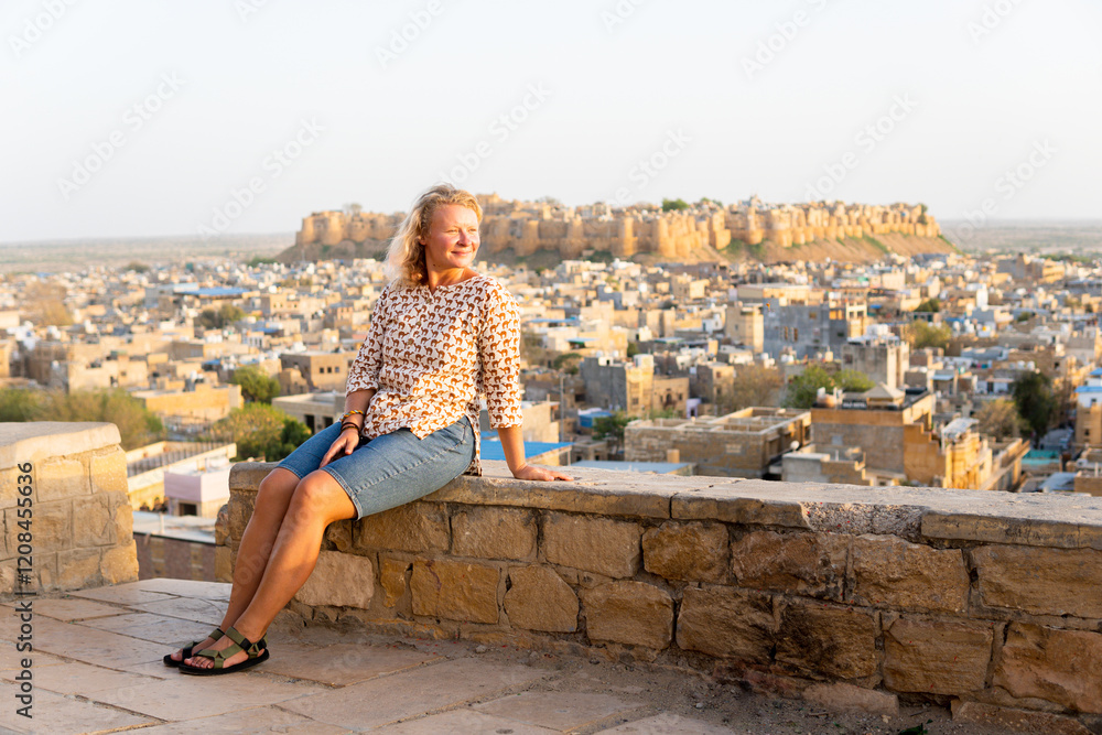 Fototapeta premium Young blonde European woman travelling in Rajasthan, enjoying panoramic view of Jaisalmer city fort, India