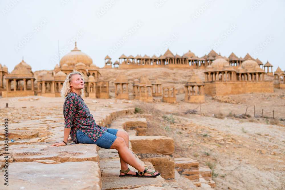 Fototapeta premium Blonde woman exploring historic Bada Bagh tombs made of sandstone in the suburbs of Jaisalmer, Rajasthan, India
