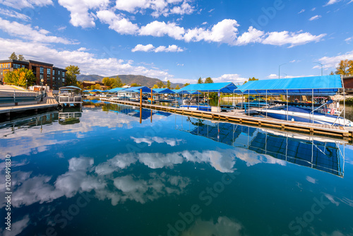 Fototapeta Naklejka Na Ścianę i Meble -  Boats in boat slips docked at the Sandpoint Marina, with the small town main street of Sandpoint Idaho behind, on Lake Pend Oreille in the North Idaho Panhandle region.	