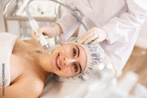 Young woman receiving facial procedure with attachment producing water with hydrogen and oxygen ions, ensuring deep penetration into dermis, relieving skin of blackheads. Modern hardware cosmetology photo