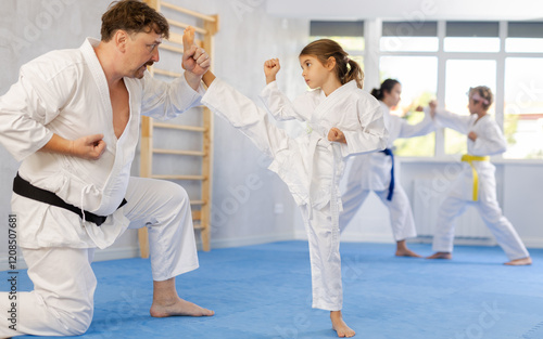 Focused preteen girl in white kimono practicing karate kicking techniques during sparring with father. Sports family activity concept photo