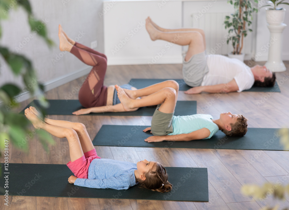 Obraz premium Sportive family members engaged in pilates lying on the floor on black mat holding legs up