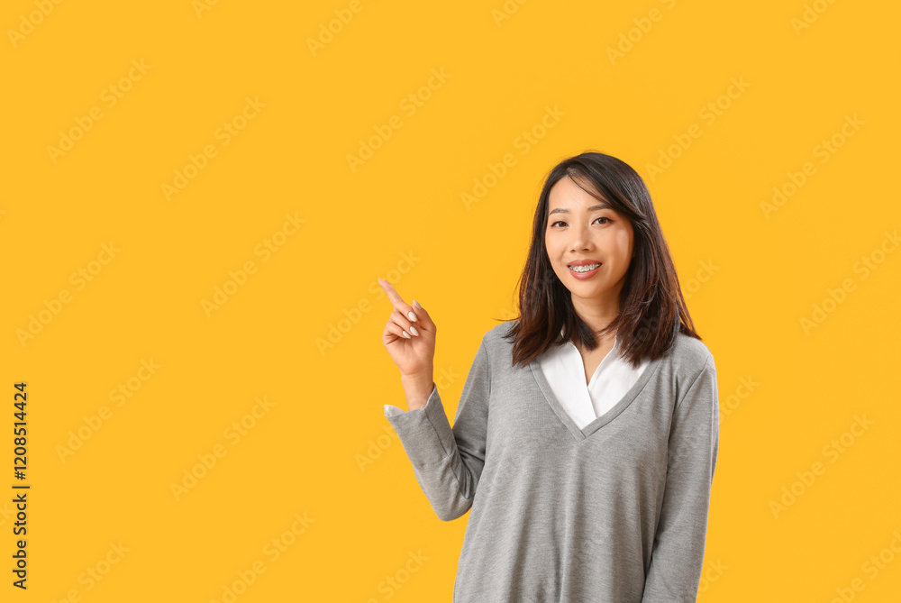 Beautiful Asian woman pointing at something on yellow background. Dialogue concept Beautiful Asian woman pointing at something on yellow background. Dialogue concept