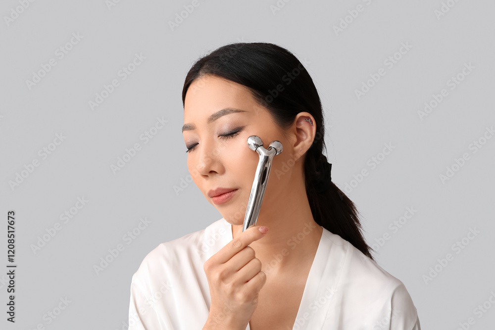 Young Asian woman in gown massaging face on light background, closeup Young Asian woman in gown massaging face on light background, closeup