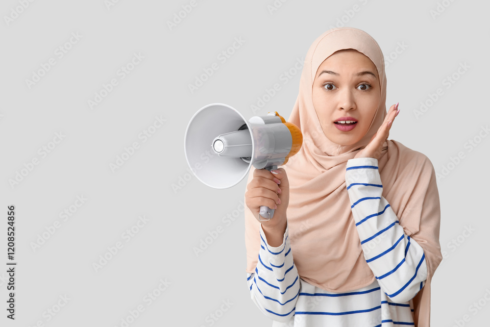 Shocked young Asian Muslim woman with megaphone on grey background. National Be Heard Day Shocked young Asian Muslim woman with megaphone on grey background. National Be Heard Day