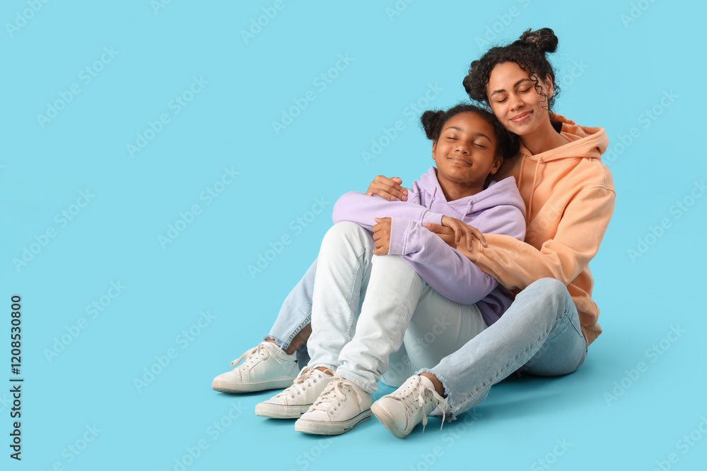 Happy young African-American woman with her daughter hugging on blue background Happy young African-American woman with her daughter hugging on blue background