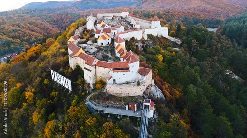 Drone footage of the iconic Râșnov Fortress perched atop a lush hill, showcasing its medieval architecture and stunning panoramic views of the surrounding Romanian countryside.