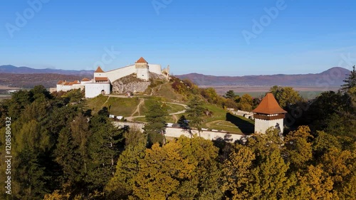 A panoramic drone shot showcasing Râșnov Fortress in its full glory, surrounded by dense forests and overlooking the charming Romanian countryside.