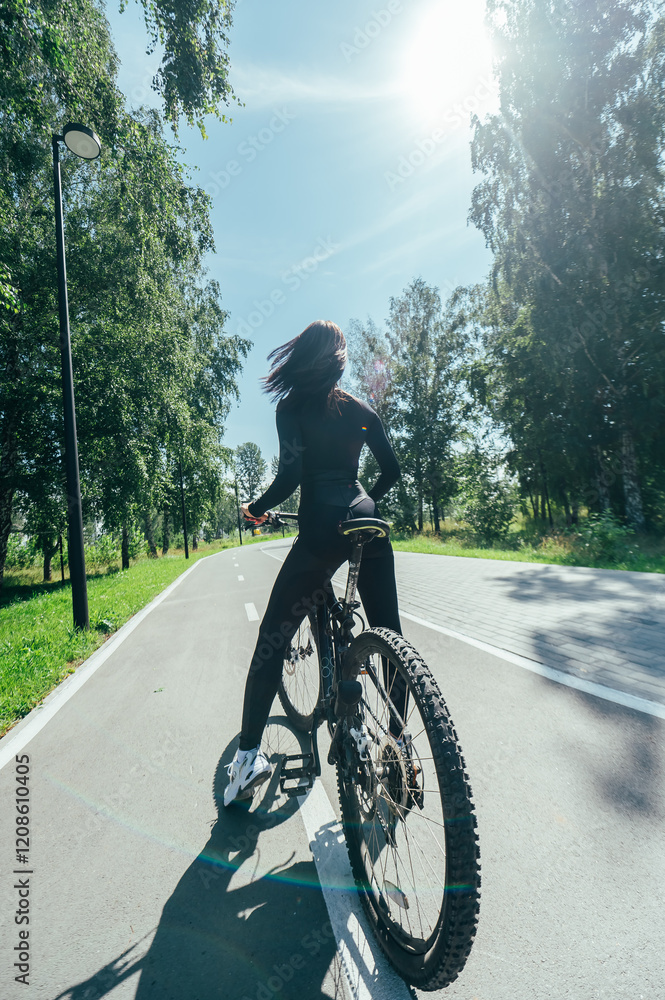 Obraz premium Rear view of Caucasian woman riding bike in park. Vertical photo. 