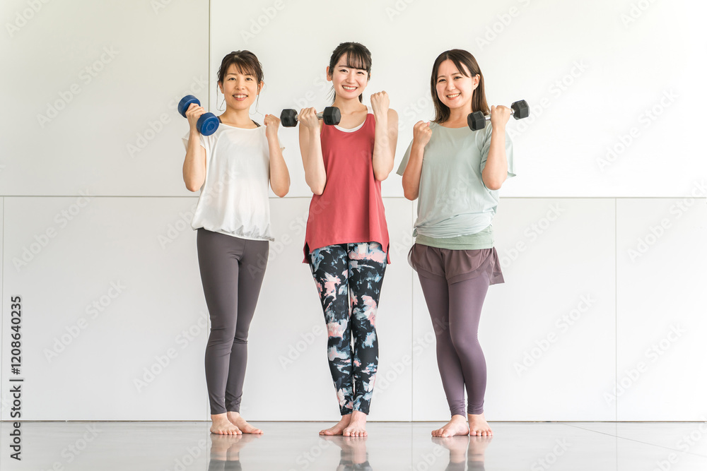 Fototapeta premium スポーツジムでダンベルを持って筋トレするスポーツウェアのアジア人の女性達 