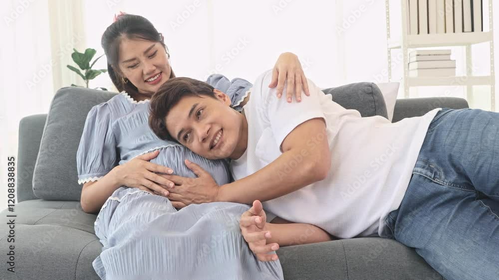 Father happy and excited about his baby in the womb hugging and touching his womb with his hands listening baby's movements and hugging his wife who is sleeping on the sofa at home. Father happy and excited about his baby in the womb hugging and touching his womb with his hands listening baby's movements and hugging his wife who is sleeping on the sofa at home.