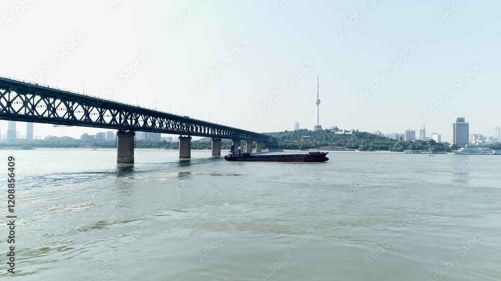 A ship slowly navigating along the Yangtze River in Wuhan, surrounded by calm waters and urban scenery A ship slowly navigating along the Yangtze River in Wuhan, surrounded by calm waters and urban scenery