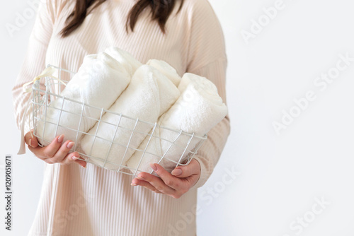 Female hands hold stylish white wire basket with white towels rolled into roll. Storage of towels. photo