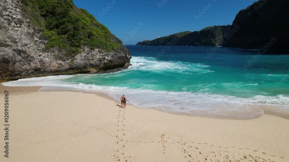 4K video of a couple holding hands, running and playing on the soft white sand by the ocean at Kelingking Beach in Nusa Penida, Bali Indonesia. The turquoise blue ocean waves crash against the shore 4K video of a couple holding hands, running and playing on the soft white sand by the ocean at Kelingking Beach in Nusa Penida, Bali Indonesia. The turquoise blue ocean waves crash against the shore