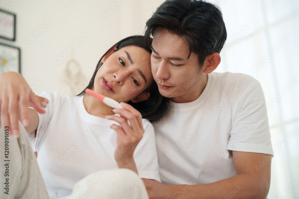 Upset Asian couple reacting to an unplanned pregnancy, woman looking distressed at a pregnancy test while man consoles her. Upset Asian couple reacting to an unplanned pregnancy, woman looking distressed at a pregnancy test while man consoles her.