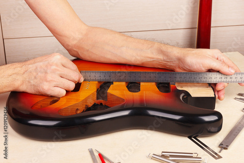 Guitar repairer measures body of guitar with ruler.